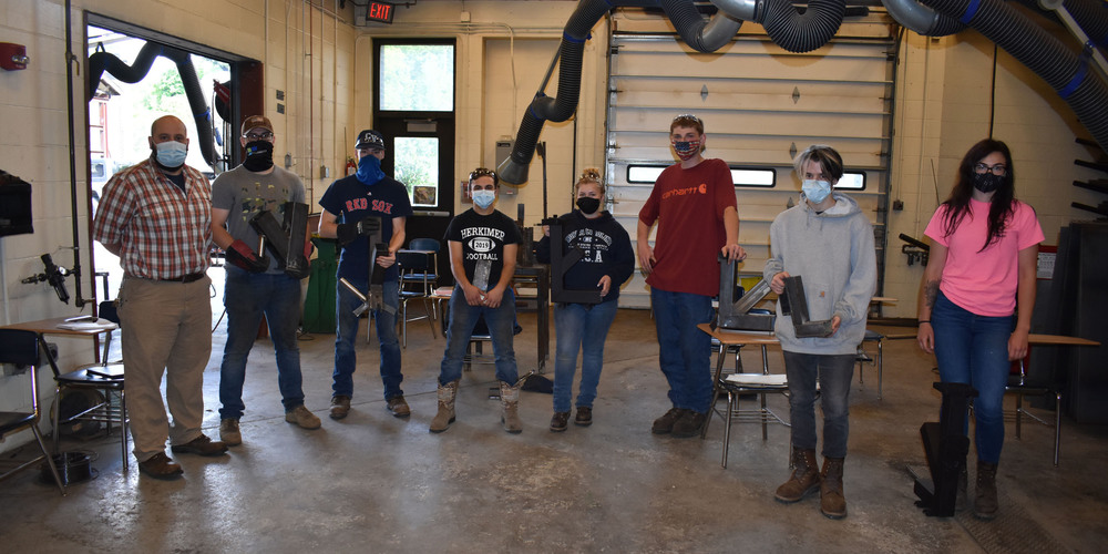 Welding instructor Mason Fisher next to Welding students holding rocket stoves they made