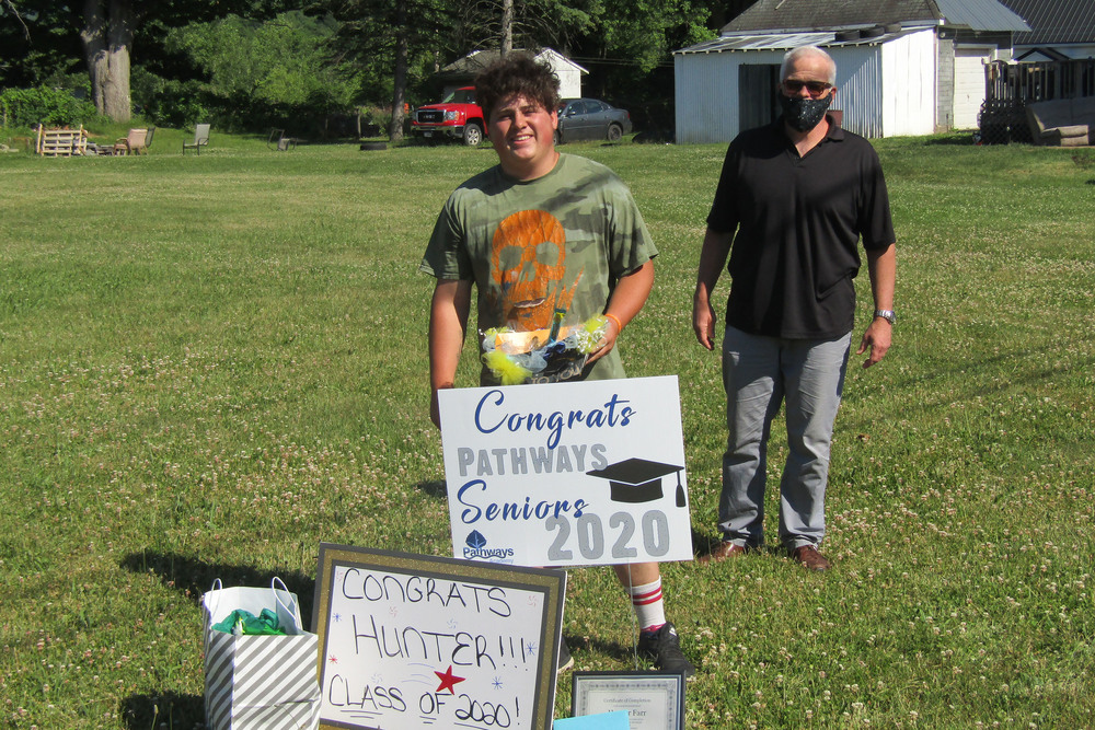 Pathways student holding a sign delivered during Senior Recognition Caravan with Patrick Corrigan standing in back