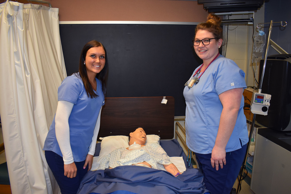 Two nursing students posing in a lab by a mannequin