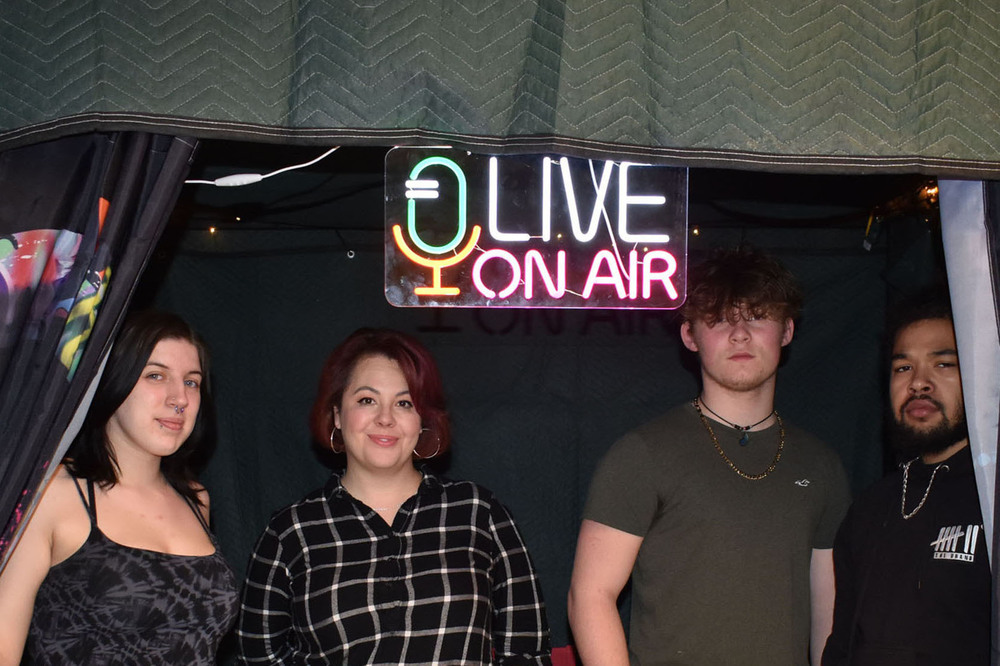 Three Pathways Academy students and English teacher in podcast recording booth with a sign that says "Live On Air"