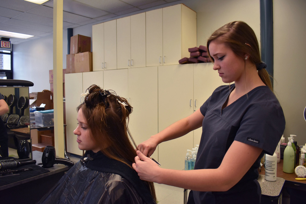 Cosmetology student standing up working on the hair of her sister who is sitting in front of her