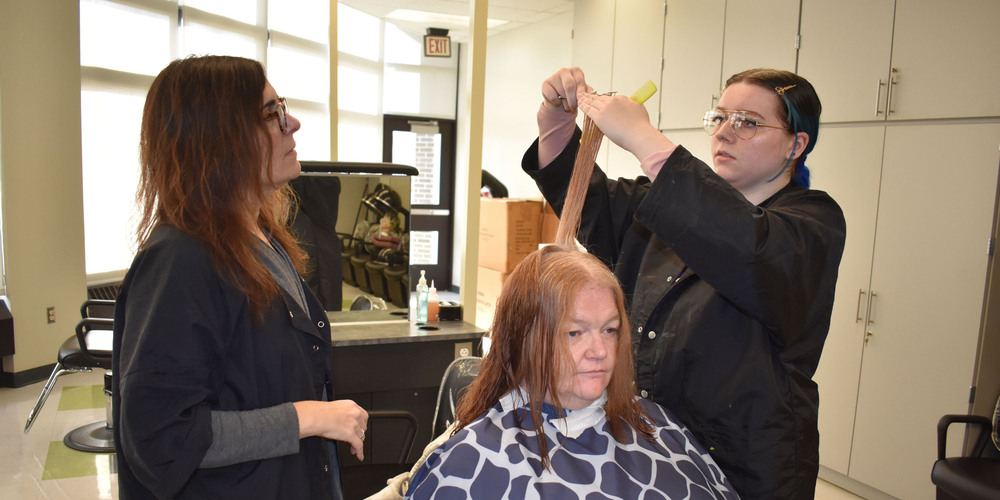 Student cutting community member's hair as instructor looks on
