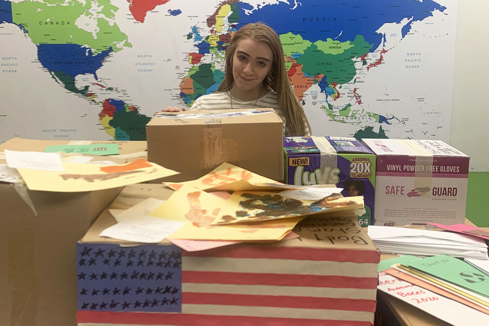 Student posing in front of map and behind boxes of donated items