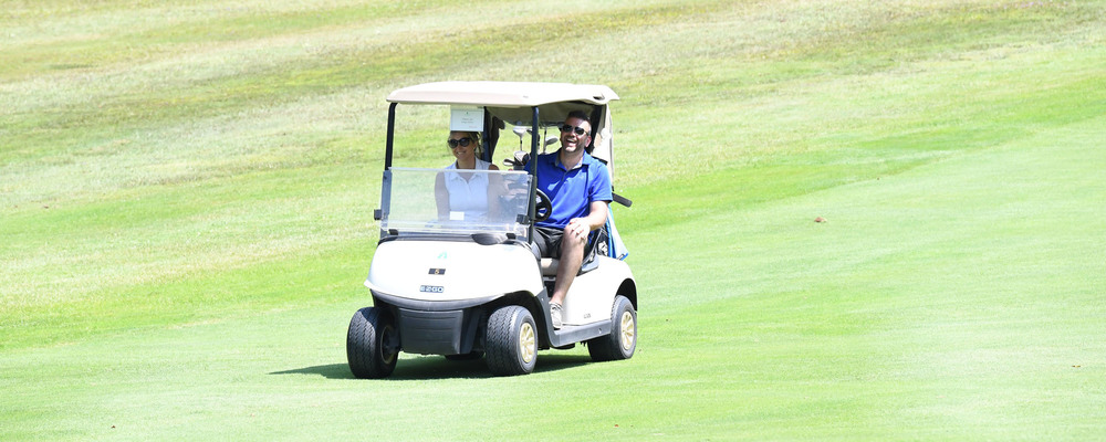 Two people smiling while riding a golf cart across the course