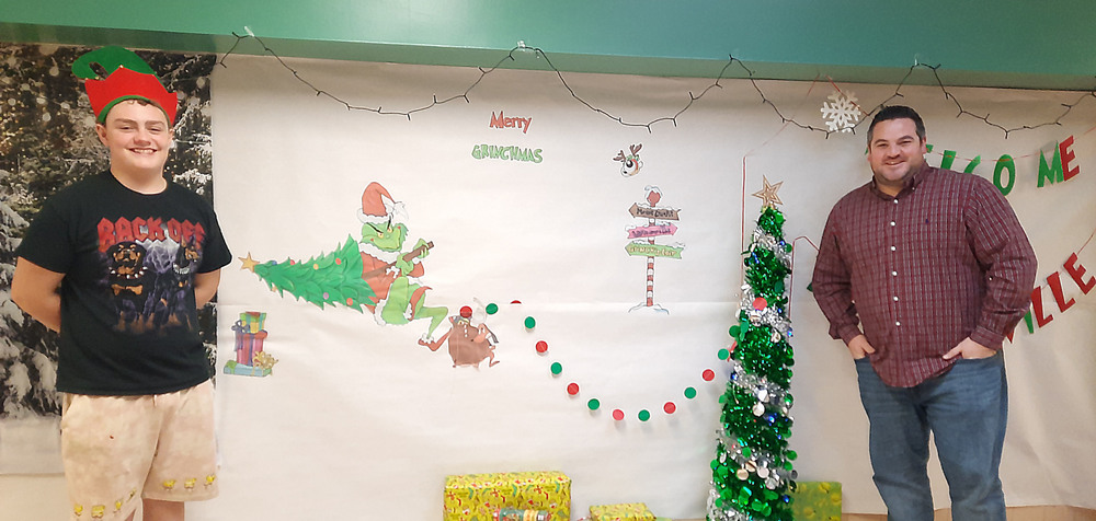 Student and teacher standing by Grinch-themed decorated wall