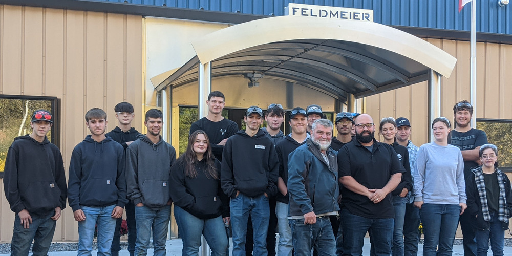 Welding seniors pose outside Feldmeier facility with instructor and plant manager