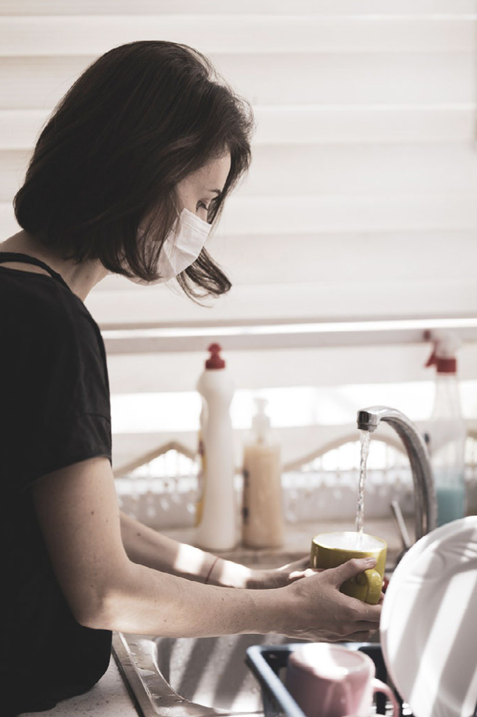 Woman washing dishes while wearing a mask