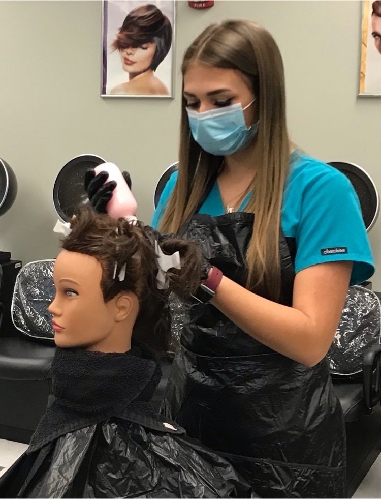 Cosmetology stuent putting gel in a mannequin's hair