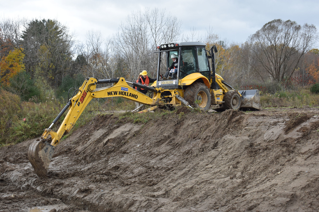 Student operating digging machinery as another student looks on