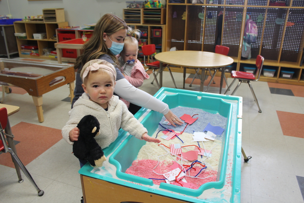 Preschool children and a Child and Family Services student play with red white and blue rice