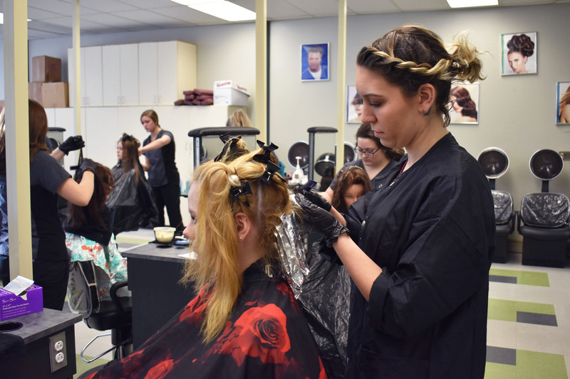 Adult cosmetology student working on the hair of another adult student sitting in front of her