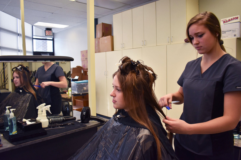 Cosmetology student standing up working on the hair of her sister who is sitting in front of her