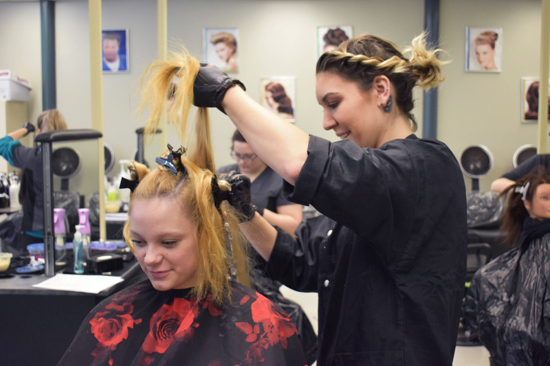 Adult cosmetology student working on the hair of another adult student sitting in front of her