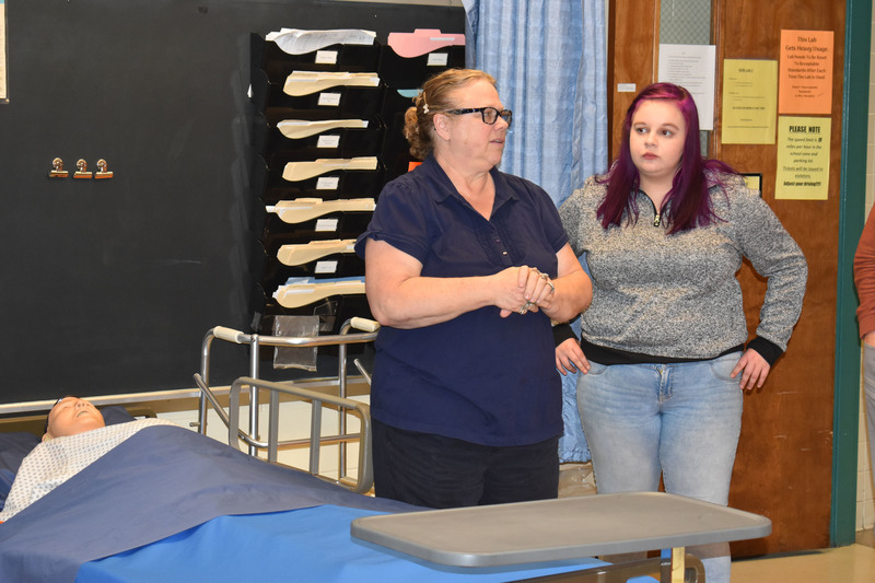 Close view of an LPN instructor and Pathways student in nursing lab talking to tour guests 