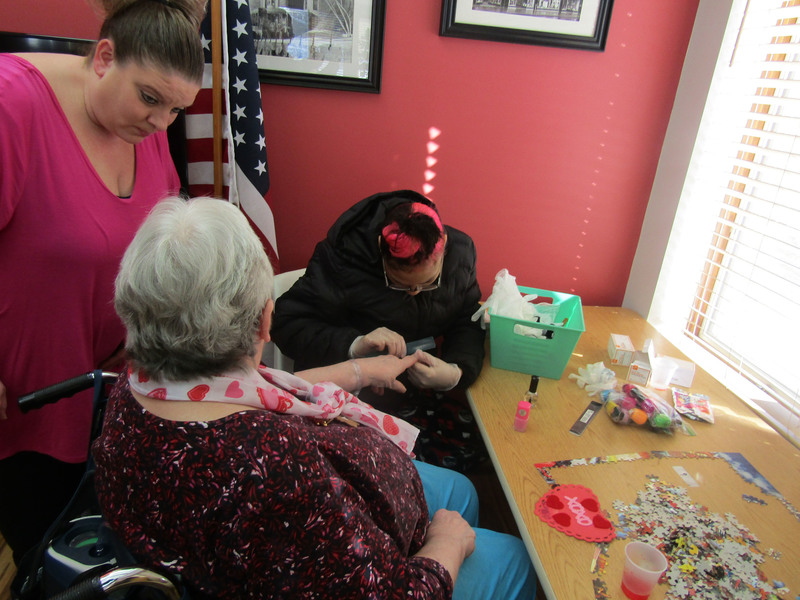 Pathways student paints a The Grand resident's nails as a Pathways teacher's assistant looks on