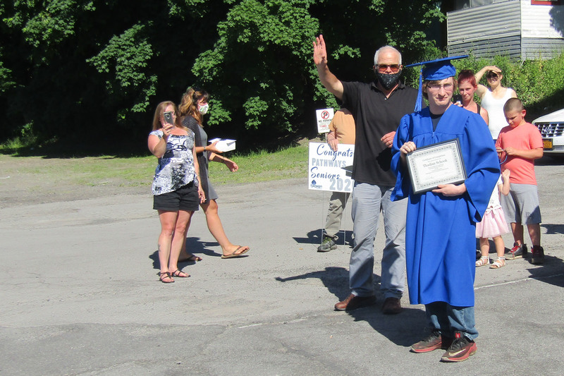 Pathways Academy student in cap and gown holding diploma from Senior Recognition Caravan with Patrick Corrigan and others nearby