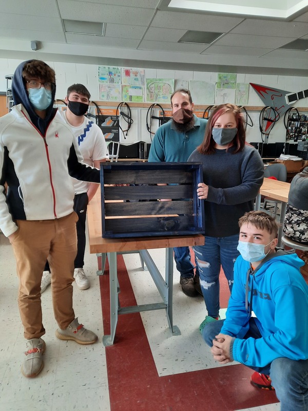 Trade Industries II teacher Adam Spatto with four students and a wooden crate the class made