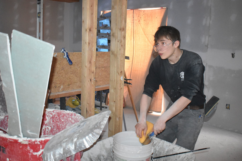 Student holding items over a bucket while working inside of a house being built