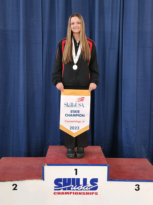 Cosmetology student holding a banner as SkillsUSA state champion in Cosmetology Jr.