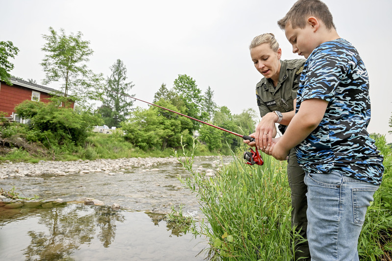 Student casts a fishing pole into Fulmer Creek with help from DEC officer