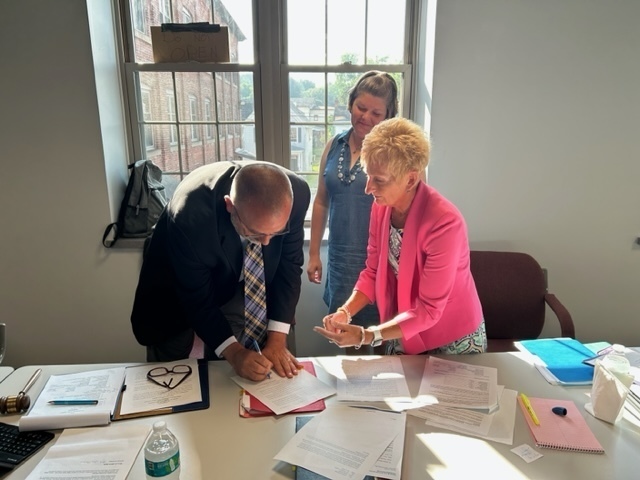 Future District Superintendent DJ Shepardson signs his contract with Shawn Maxson and Holly Pullis