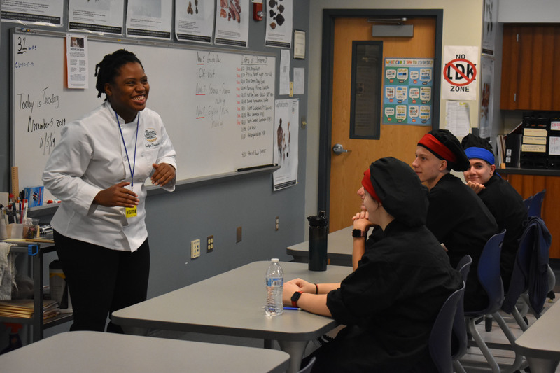 Culinary Institute of America chef laughs while talking in classroom to Culinary Hospitality students